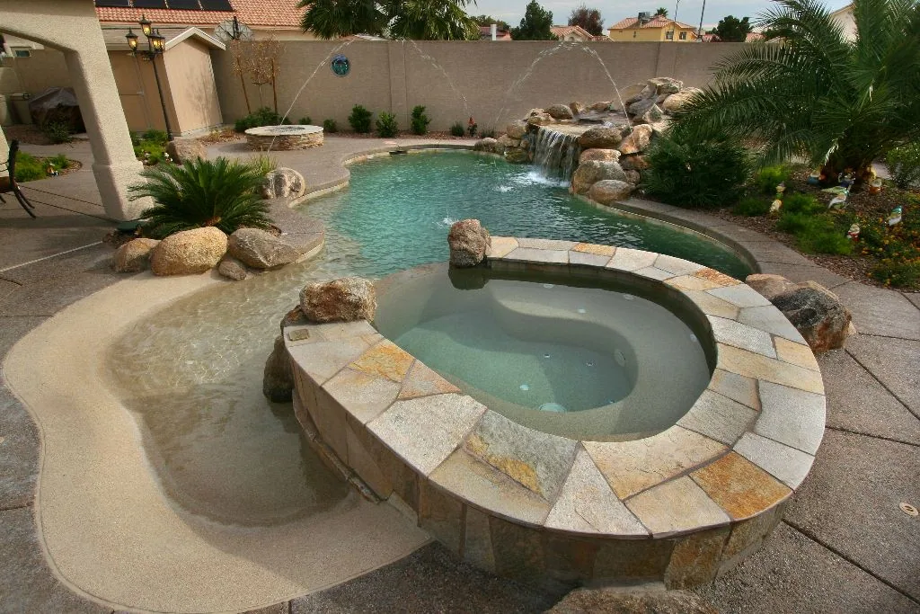 Piscina de arena con spa circular, cascada de roca y jardín